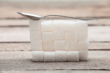 The refined sugar put by a pyramid on a wooden table from old boards, with a teaspoon.