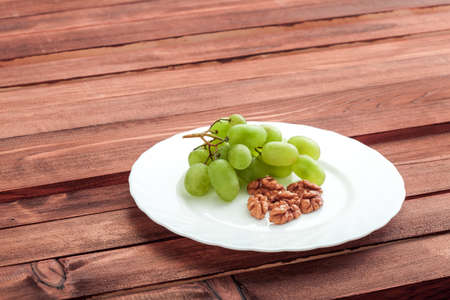 Green grapes in a white plate with a walnut on a table with wooden texture.の写真素材