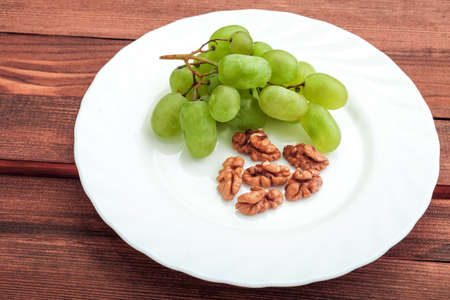 Green grapes in a white plate with a walnut on a table with wooden texture.の写真素材