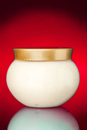Glass jar of cream for care of a body and personal hygiene on a red background with reflection, nobody.の写真素材