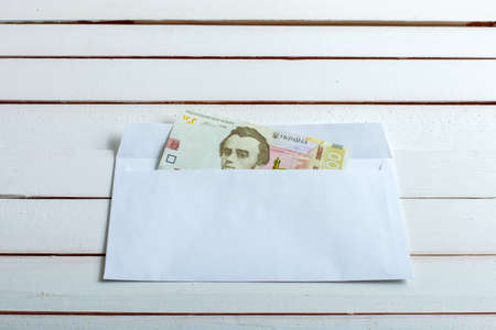 Cash in an envelope, the denomination of ukrainian hryvnia on a table from white wooden boards.の写真素材