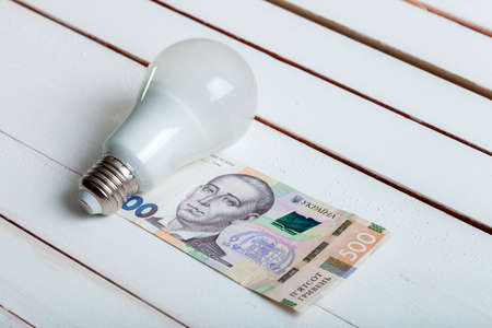 led bulb with money lies on a white wooden table from board.の写真素材