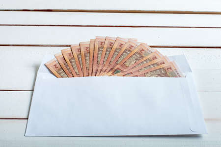 Cash in an envelope, the denomination of ukrainian hryvnia on a table from white wooden boards.の写真素材