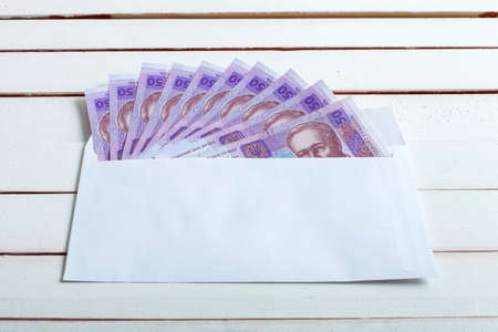 Cash in an envelope, the denomination of ukrainian hryvnia on a table from white wooden boards.の写真素材