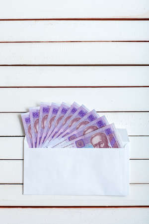 Cash in an envelope, the denomination of ukrainian hryvnia on a table from white wooden boards.の写真素材