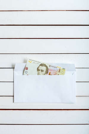 Cash in an envelope, the denomination of ukrainian hryvnia on a table from white wooden boards.の写真素材