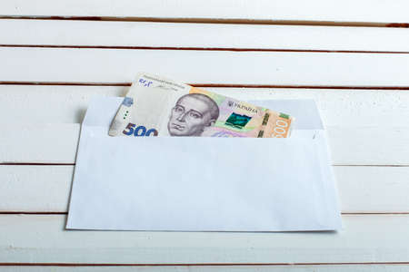 Cash in an envelope, the denomination of ukrainian hryvnia on a table from white wooden boards.の写真素材