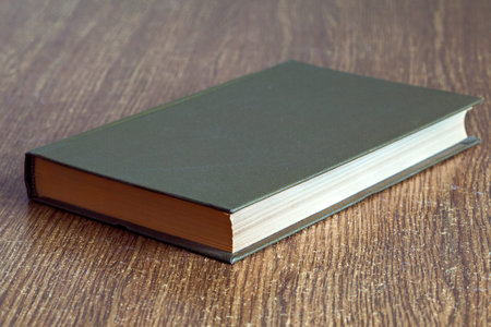 The book in firm cover lies on a table with wooden texture.