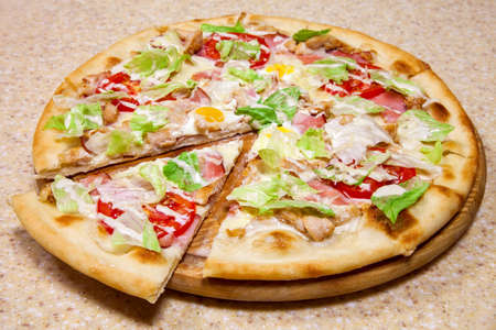 Vegetables and meat pizza on a round wooden plate lies on a table.の写真素材