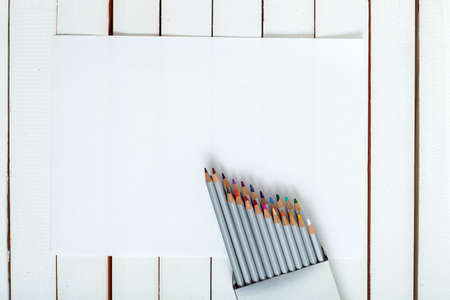 several colored pencils which are looking out of a pack which are on the sheet of paper lying on a wooden table from white board.の写真素材