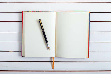 the ink handle lies on empty pages of a notebook with blank sheets which lies on white wooden board, a fountain pen from a notebook on a table.の写真素材