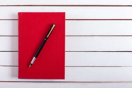 the ink handle lies on red book hard back. which lies on white wooden board, a fountain pen from a book on a table.の写真素材