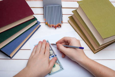 On a wooden table hardcover books with a pencil and the sheet of paper on which in hands the pencil draw.の写真素材