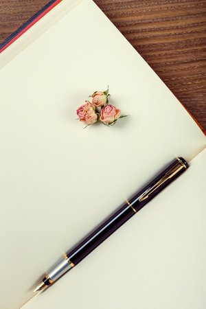 the ink handle lies on empty pages of a notebook with blank sheets which lies on wooden table, a fountain pen from a book with rose.の写真素材