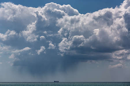 The sea horizon, the sky with a cloud over the ship floating by sea, on the ship it is raining.の写真素材