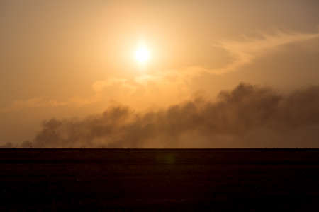 On the horizon in are far a smoke column from the fire at sunset.の写真素材