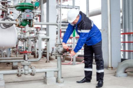 The blurred background, the engineer in a uniform with a helmet on the head performs turns the valve...