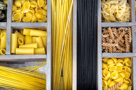 assortment of pasta in a wooden box with cells for different types of products top view on the traditional Italian food.の写真素材