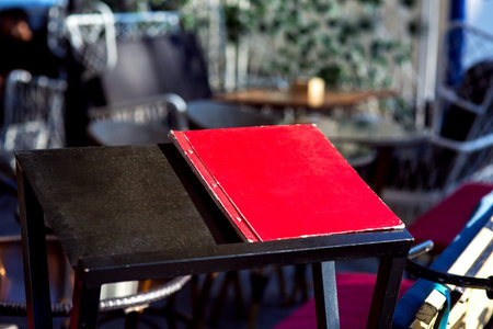 A black wooden stand on which lies a red folder with a restaurant menu on the background of empty...