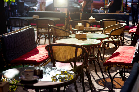 Outdoor cafe with soft seats and glass tables with a sun flare, an empty cafe and people with cars in the background of the restaurant.の写真素材