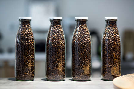 Glass transparent bottles filled with roasted coffee beans, transparent containers with a white lid stand on the table of the store's matrine.の写真素材