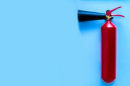 An iron extinguisher of red color is installed against the background of a blue wall with a free...