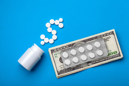 dollar symbol from pills near a bottle of medicine and expensive drugs lying on a paper bill of cash...