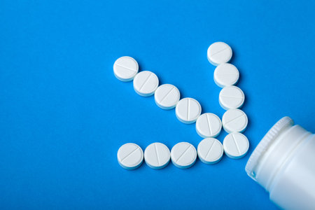 Round white tablets laid out in the shape of an arrow indicate a plastic bottle on a blue...
