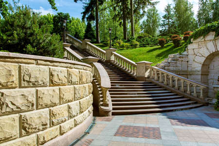 stone wall near the marble staircase with balustrades and iron lanterns against a landscape with green plants in the park garden of the mansion.の写真素材