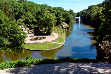 Park with a pond and a flowerbed among the stone cliffs and high green trees of the park for...