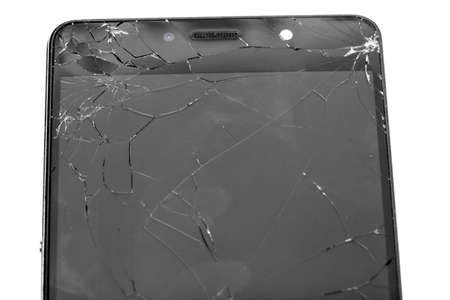 The upper part of the broken smartphone with cracks on the glass of the screen close-up on a white background.の写真素材