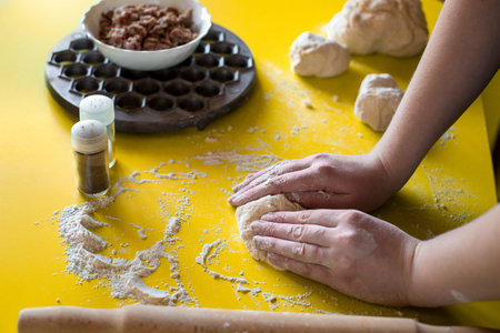 the hands of the cook knead the dough on a yellow floured table near the form for ravioli with a...
