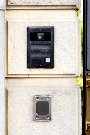 An intercom with a call button and a camera with a microphone on a stone wall with a rusticate on...