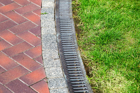 curve iron gutter with grate to the drainage system on the side of the walkway with green lawn on...