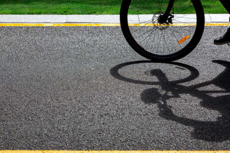A bicycle wheel rides along an asphalt road and cast a shadow, on highway with yellow markings on a sunny summer day with copy space.の写真素材