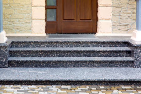 entrance threshold with marble steps to a wooden door with a rubber mat and a stone facade and rustication.の写真素材