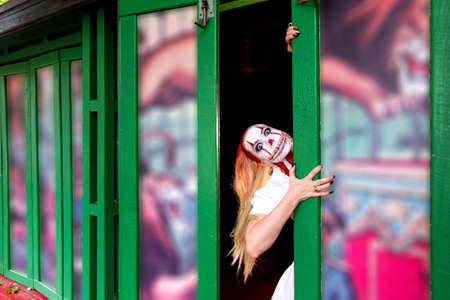 portrait of a crazy clown makeup girl with red hairstyle with scary venom teeth and hysterical look with red eyes in a frame, the image of a woman on the theme of halloween.の写真素材