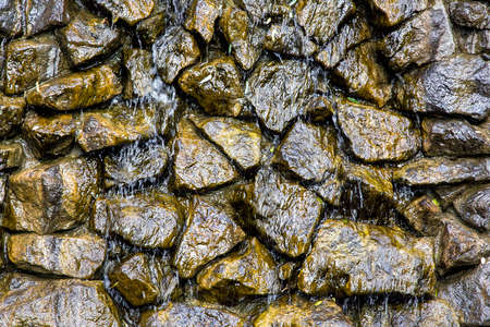 artificial waterfall from a pile of stone water flowing down it, close up of wet blocks of stones.の写真素材