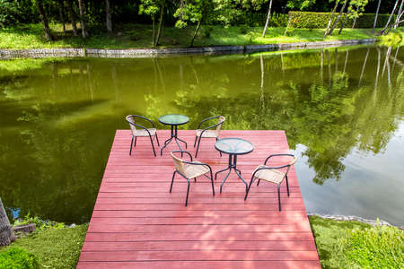 cafe on a wooden pier of red boards with tables and chairs on the river bank with a green plant, nobody.の写真素材