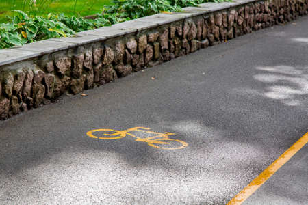 asphalt road with yellow markings and a bicycle symbol, closeup of the road surface in the shade with spots of sunlight.の写真素材