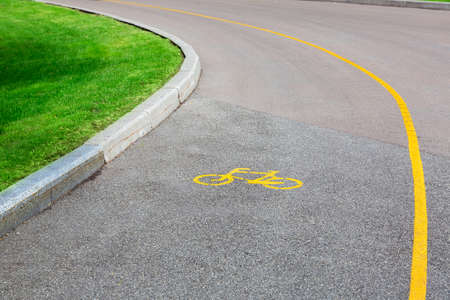 Bicycle symbol on an asphalt road with a dedicated lane for bicycle traffic, an empty road with a curb and green grass on the side of the road.の写真素材