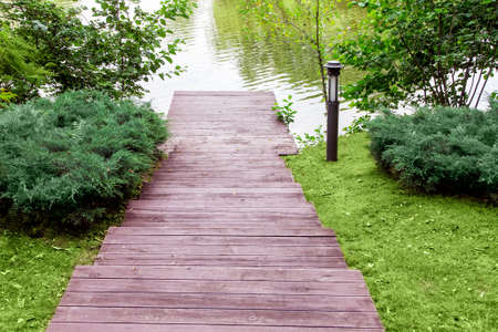 wooden steps down to the pier on the river, a slope with a landscape of green bushes and a lawn with a lantern, view from above.の写真素材
