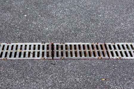 iron grid drainage system on an asphalt road, closeup.の写真素材