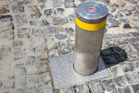hydraulic gray electric bollard with a yellow reflective strip on the old stone tile road on a sunny day.の写真素材