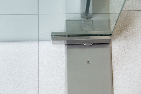 Glass door fittings, swivel mechanism holding the door metal loop on the tile floor close up detail.の写真素材