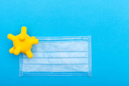 medical mask with yellow virus bacterium on a blue background with copy space, conceptual background on a medical theme mock up top view.の写真素材