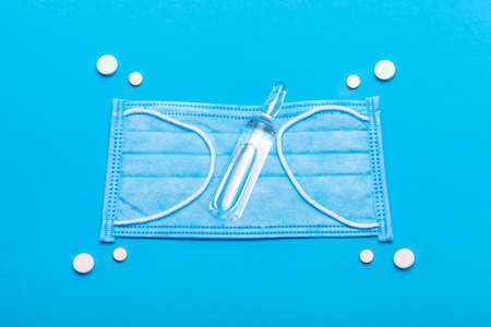 concept medical mock up with drugs to protect health and treatment against viruses, close up of a sick mask and pills with a vaccine on a blue background with copy space.の写真素材