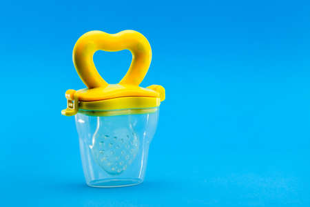 Fruit feeder in a plastic case with a yellow handle and a silicone pacifier on a blue background with a copy space.の写真素材