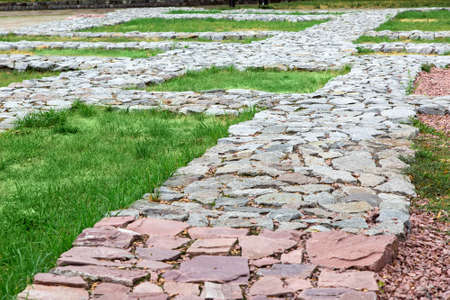 footpaths made of natural rough stone paved with mosaic in the lawn grass in the old town.の写真素材