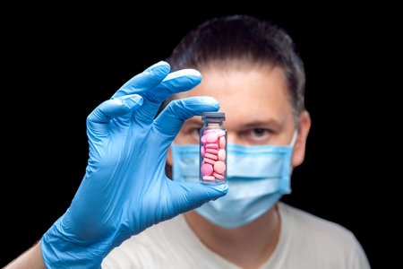 male portrait a doctor in a medical mask holds in hand on sterile glove a glass bottle with pink...